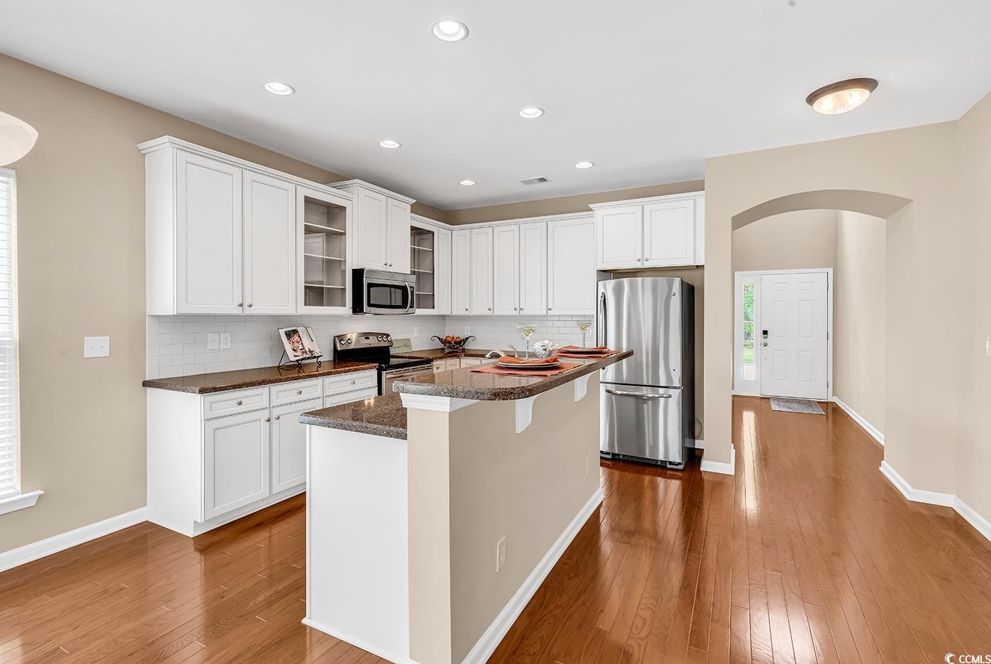 126 Dreamland Drive Murrells Inlet, SC 29576 - Photo 6 of 40 Kitchen with appliances with stainless steel finishes, dark wood-style floors, glass insert cabinets, backsplash, and white cabinetry