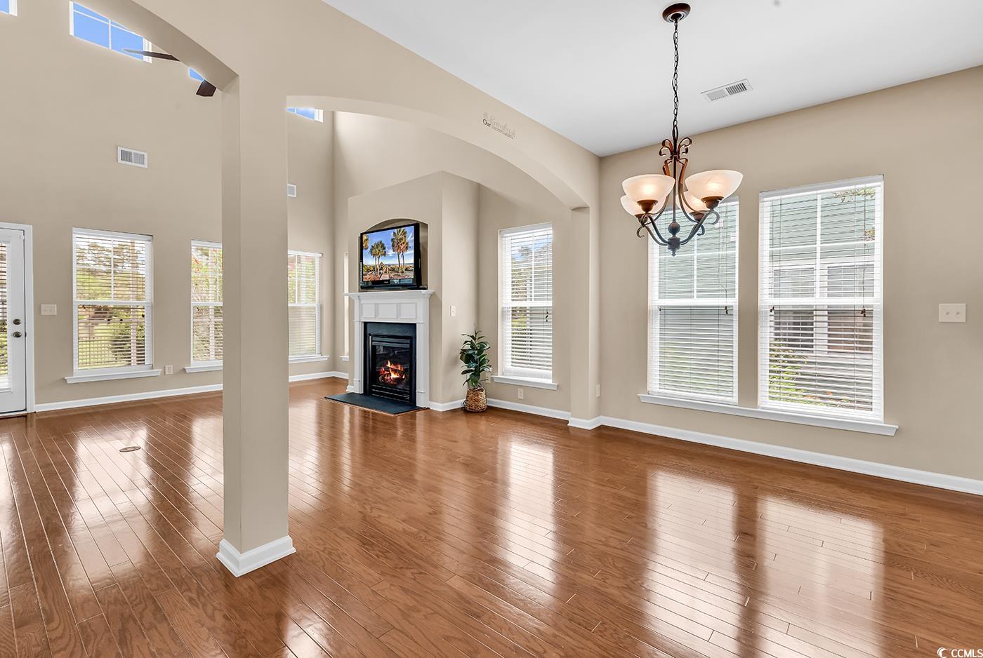126 Dreamland Drive Murrells Inlet, SC 29576 - Photo 8 of 40 Unfurnished living room featuring baseboards, a chandelier, a glass covered fireplace, and wood finished floors