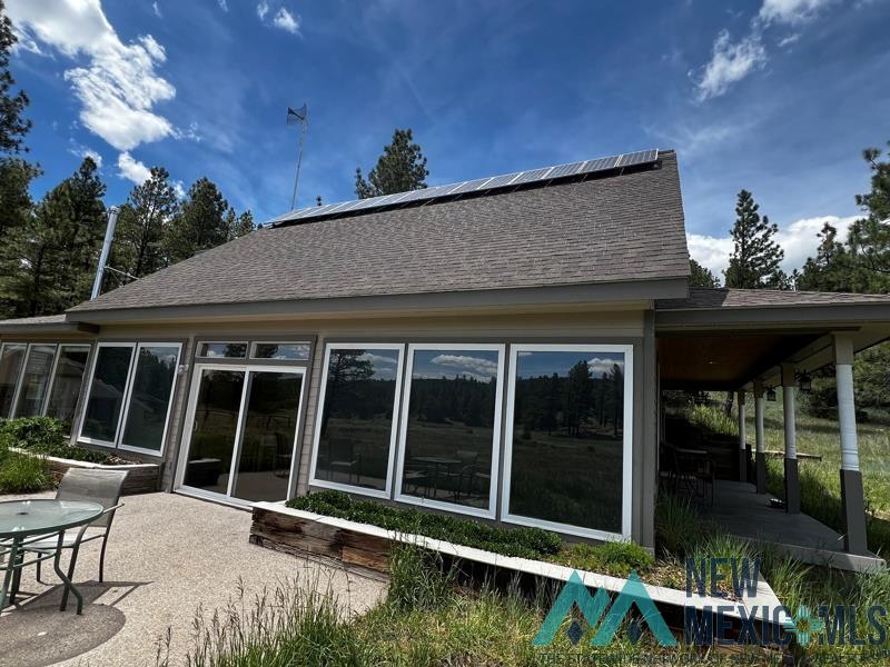 150 Forrest Service Road 124 Road Chamisal, NM 87521 - Photo 3 of 42 Rear view of house featuring roof with shingles, a patio area, a sunroom, and solar panels