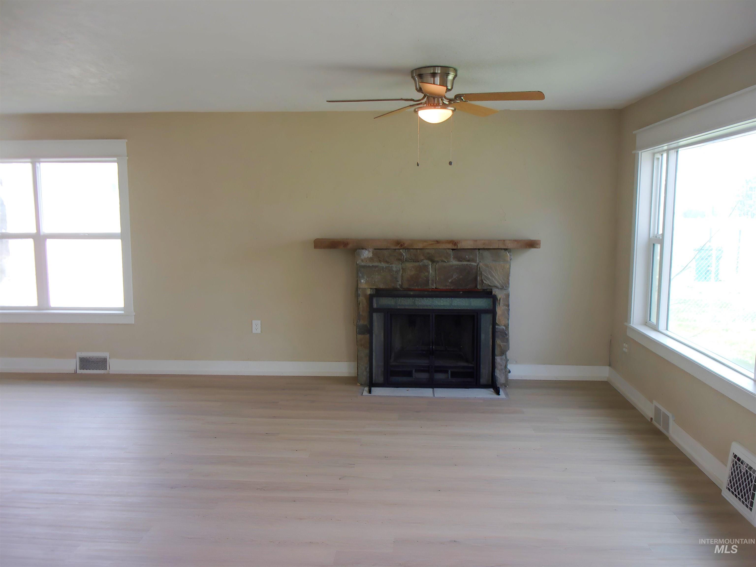 605 North 6th Street Parma, ID 83660 - Photo 8 of 46 Unfurnished living room featuring healthy amount of natural light, light wood finished floors, a stone fireplace, and ceiling fan