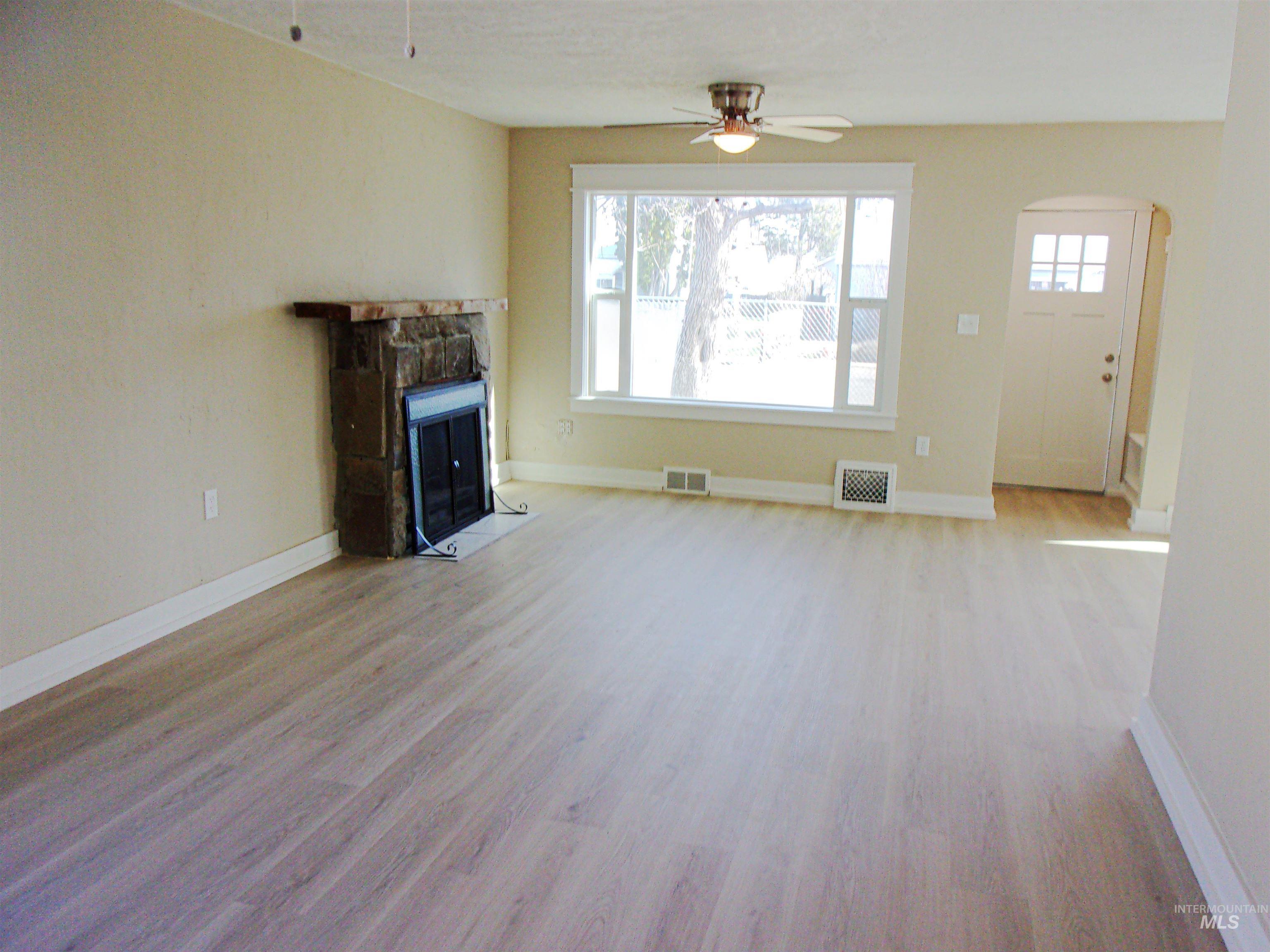 605 North 6th Street Parma, ID 83660 - Photo 10 of 46 Unfurnished living room featuring light wood finished floors, arched walkways, a ceiling fan, and a stone fireplace
