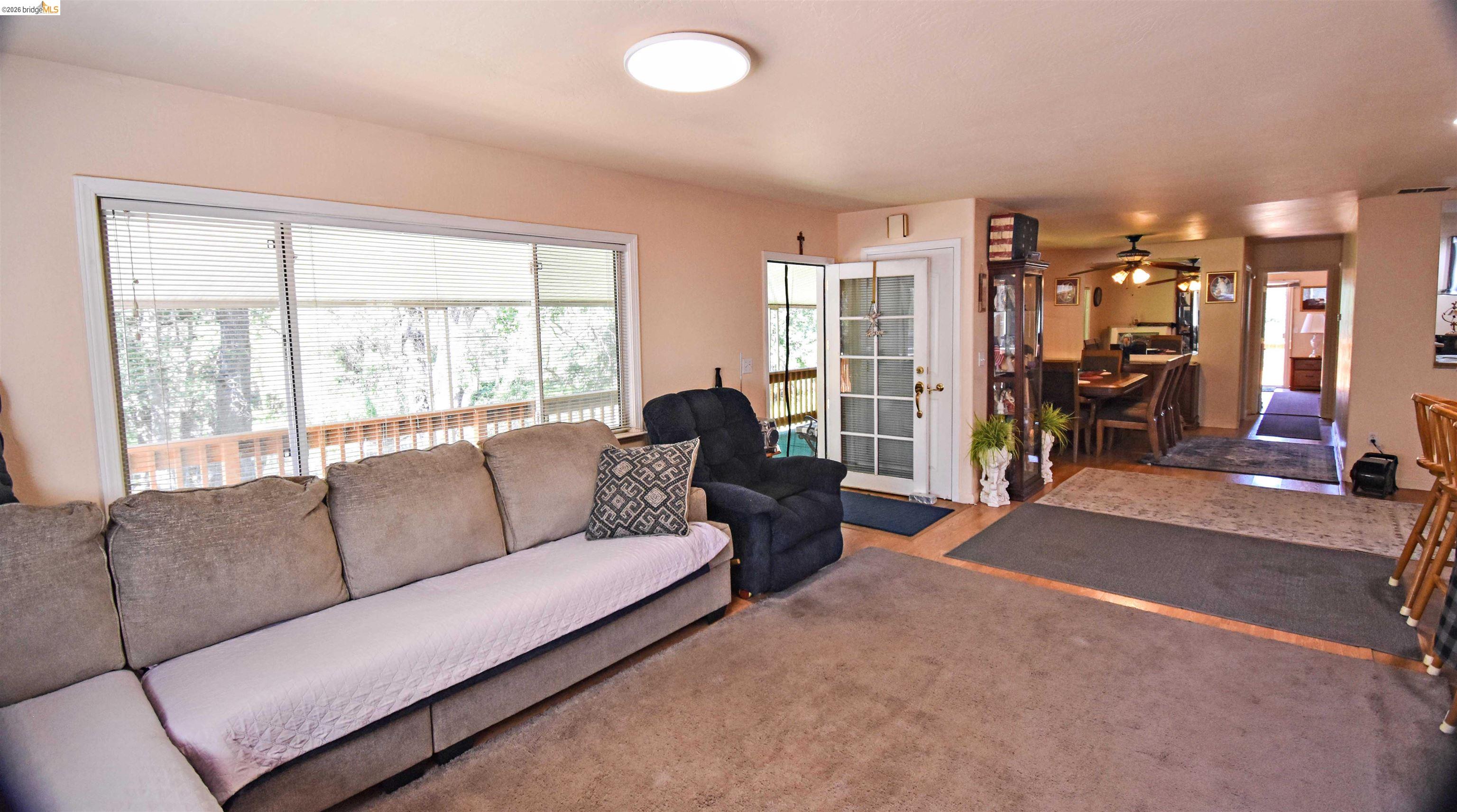 13904 Tuolumne Road Sonora, CA 95370 - Photo 11 of 44 Living area featuring a large window, light-colored walls, carpeted flooring, and a glass-paned door opening to an outdoor deck