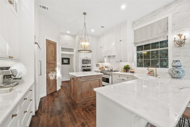 a open kitchen with stainless steel appliances kitchen island granite countertop a stove a sink a refrigerator and white cabinets with wooden floor
