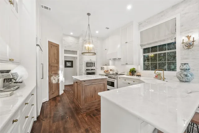 a open kitchen with stainless steel appliances kitchen island granite countertop a stove a sink a refrigerator and white cabinets with wooden floor