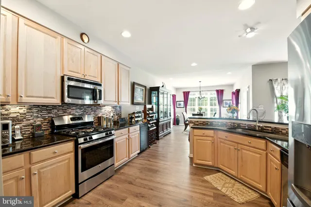 a kitchen with stainless steel appliances a stove top oven a sink a refrigerator white cabinets and wooden floor