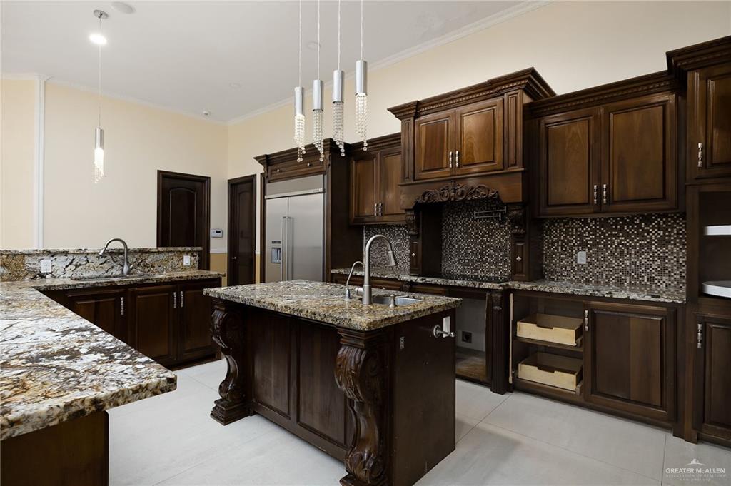 22111 Uresti Road Edinburg, TX 78542 - Photo 10 of 38 Kitchen featuring dark wood cabinetry, multi-toned granite countertops, a mosaic tile backsplash, and stainless steel appliances