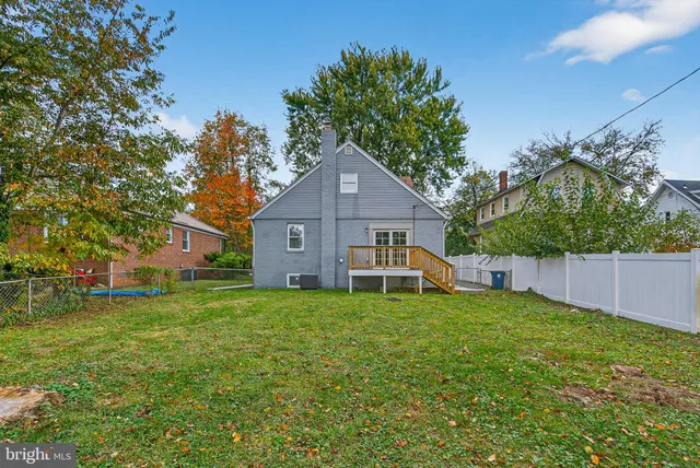 a house that is sitting in the grass with large trees and plants