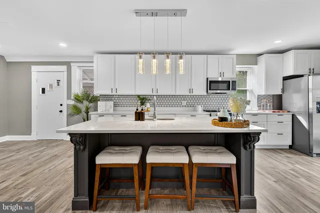 a kitchen with stainless steel appliances kitchen island granite countertop a dining table chairs and a refrigerator