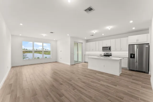 a view of kitchen with stainless steel appliances refrigerator oven and white cabinets with wooden floor