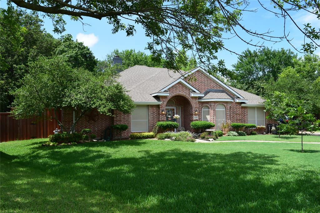 4201 Glistening Spring Rowlett, TX 75088 - Photo 1 of 33 Traditional brick exterior featuring a covered entry, arched window details, a gabled roofline, and established landscaping with mature trees