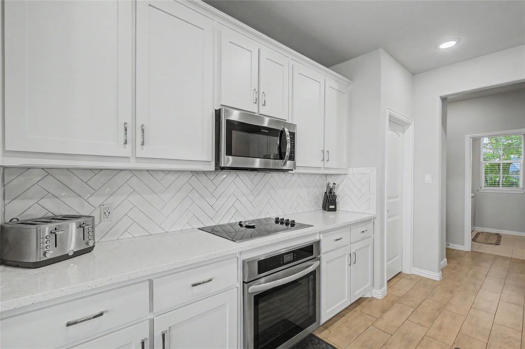 185 Chester Road Springtown, TX 76082 - Photo 20 of 40 Modern kitchen featuring white shaker cabinetry, stainless steel appliances, a white herringbone tile backsplash, and light-toned countertops