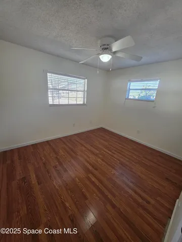 an empty room with wooden floor chandelier fan and windows