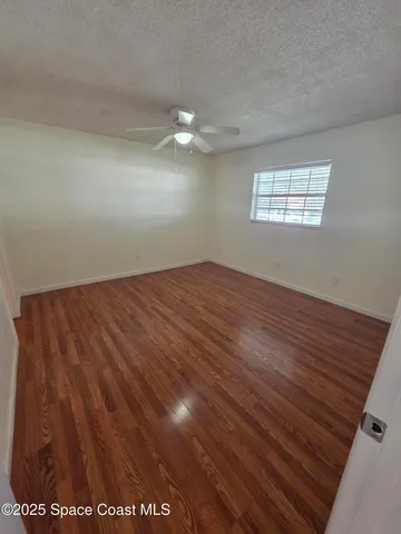 an empty room with wooden floor fan and windows