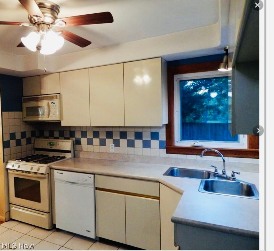 Kitchen with white appliances, backsplash, sink, light tile flooring, and ceiling fan