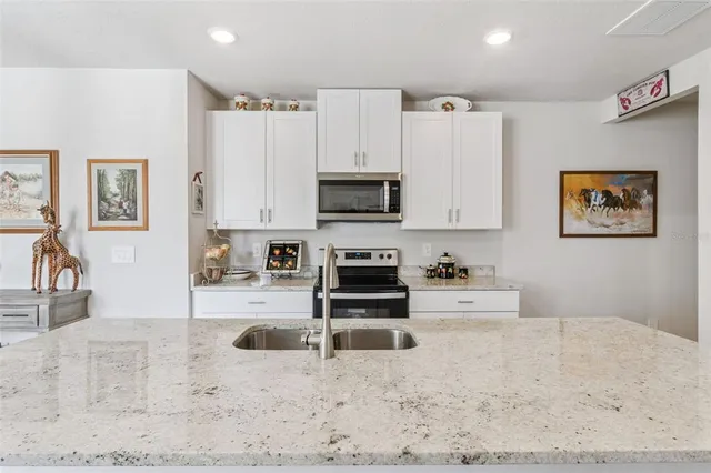 a kitchen with stainless steel appliances a stove a sink a refrigerator white cabinets and wooden floor