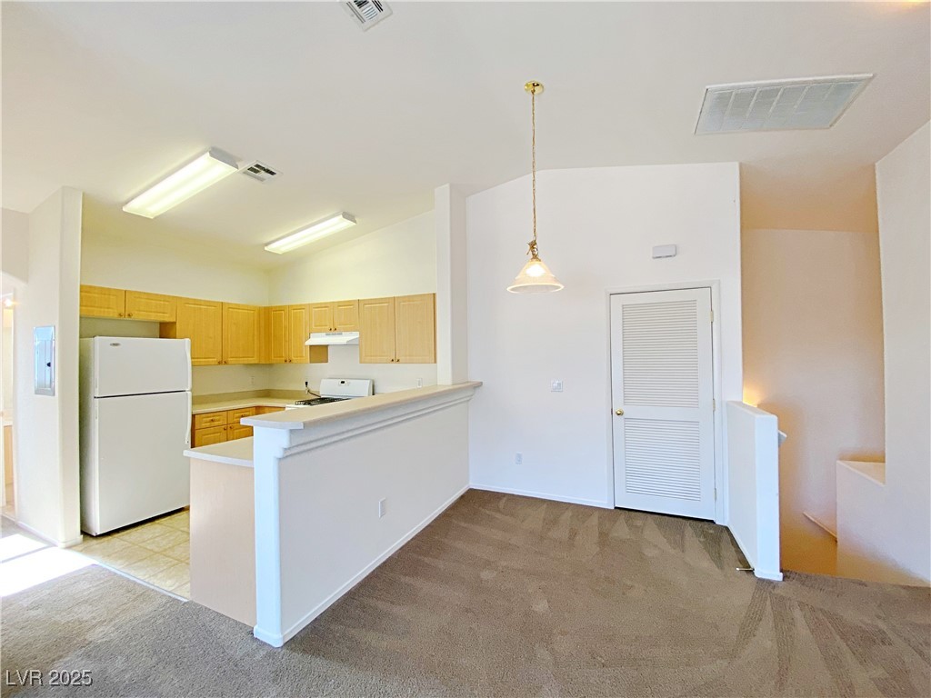 9335 Indian Corn Court, Unit 101 Las Vegas, NV 89178 - Photo 5 of 18 Kitchen featuring white appliances, light carpet, light countertops, lofted ceiling, and a peninsula
