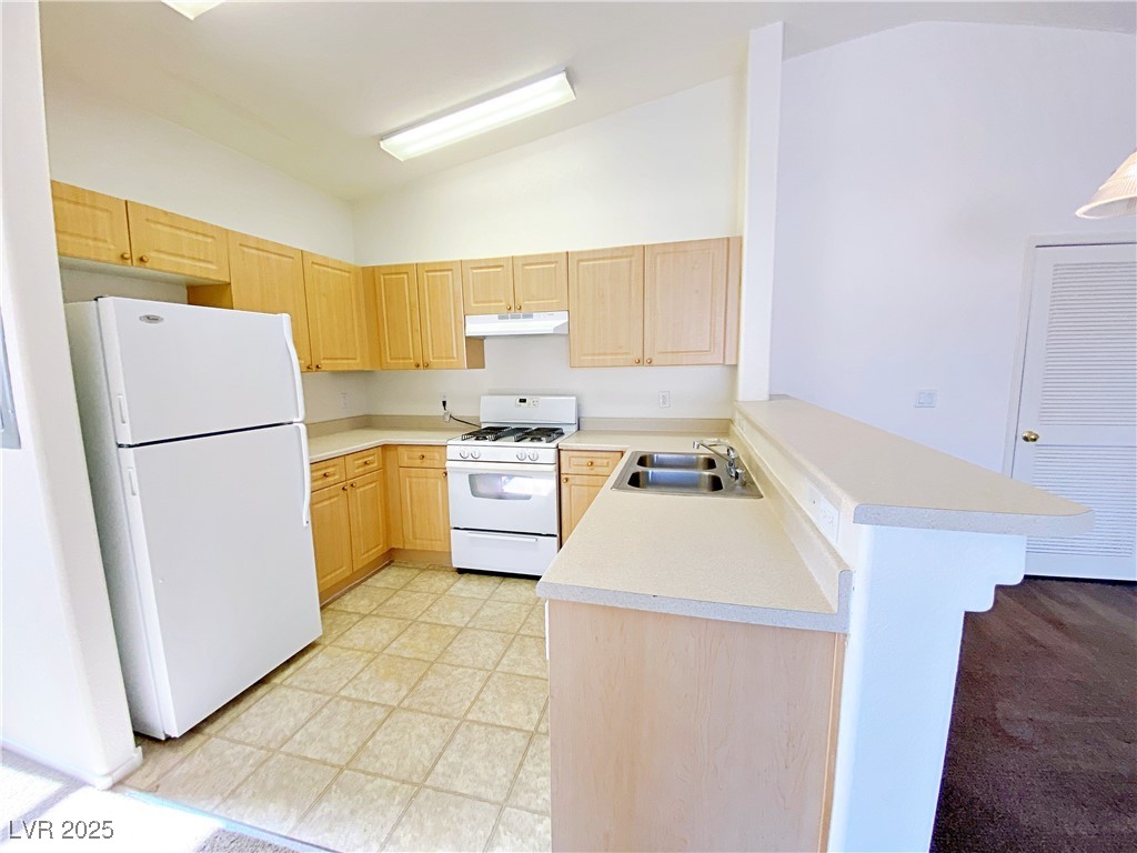 9335 Indian Corn Court, Unit 101 Las Vegas, NV 89178 - Photo 7 of 18 Kitchen featuring light brown cabinetry, vaulted ceiling, white appliances, a peninsula, and light countertops