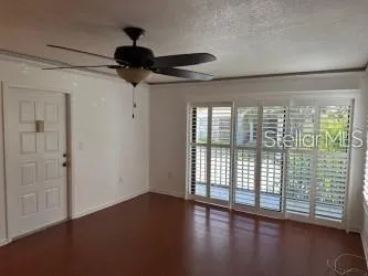 a view of an empty room with wooden floor and a ceiling fan