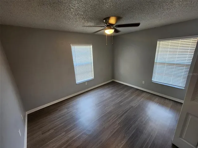 an empty room with wooden floor fan and windows