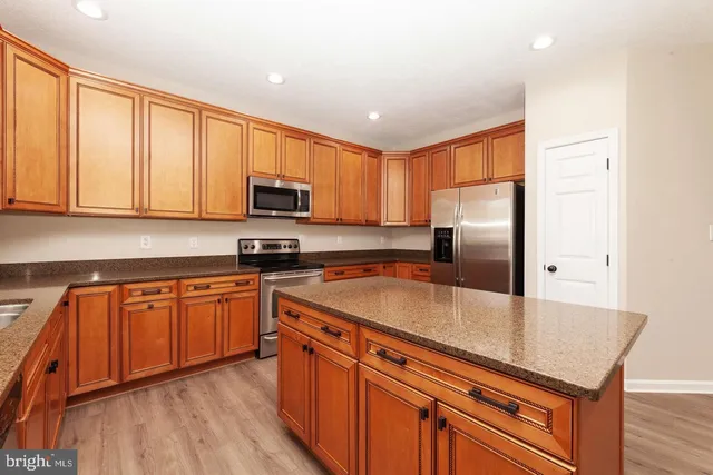 a kitchen with stainless steel appliances granite countertop a stove a sink dishwasher and a refrigerator with wooden floor