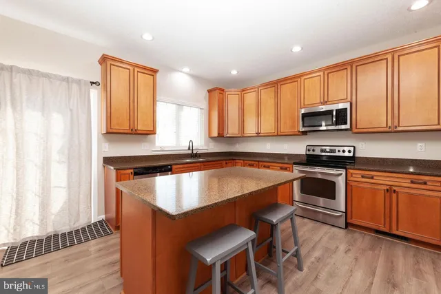 a kitchen with stainless steel appliances granite countertop wooden cabinets a stove top oven a sink and dishwasher with wooden floor