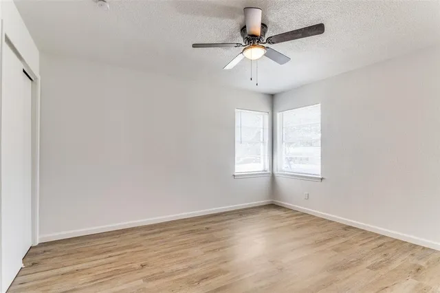 an empty room with wooden floor fan and windows