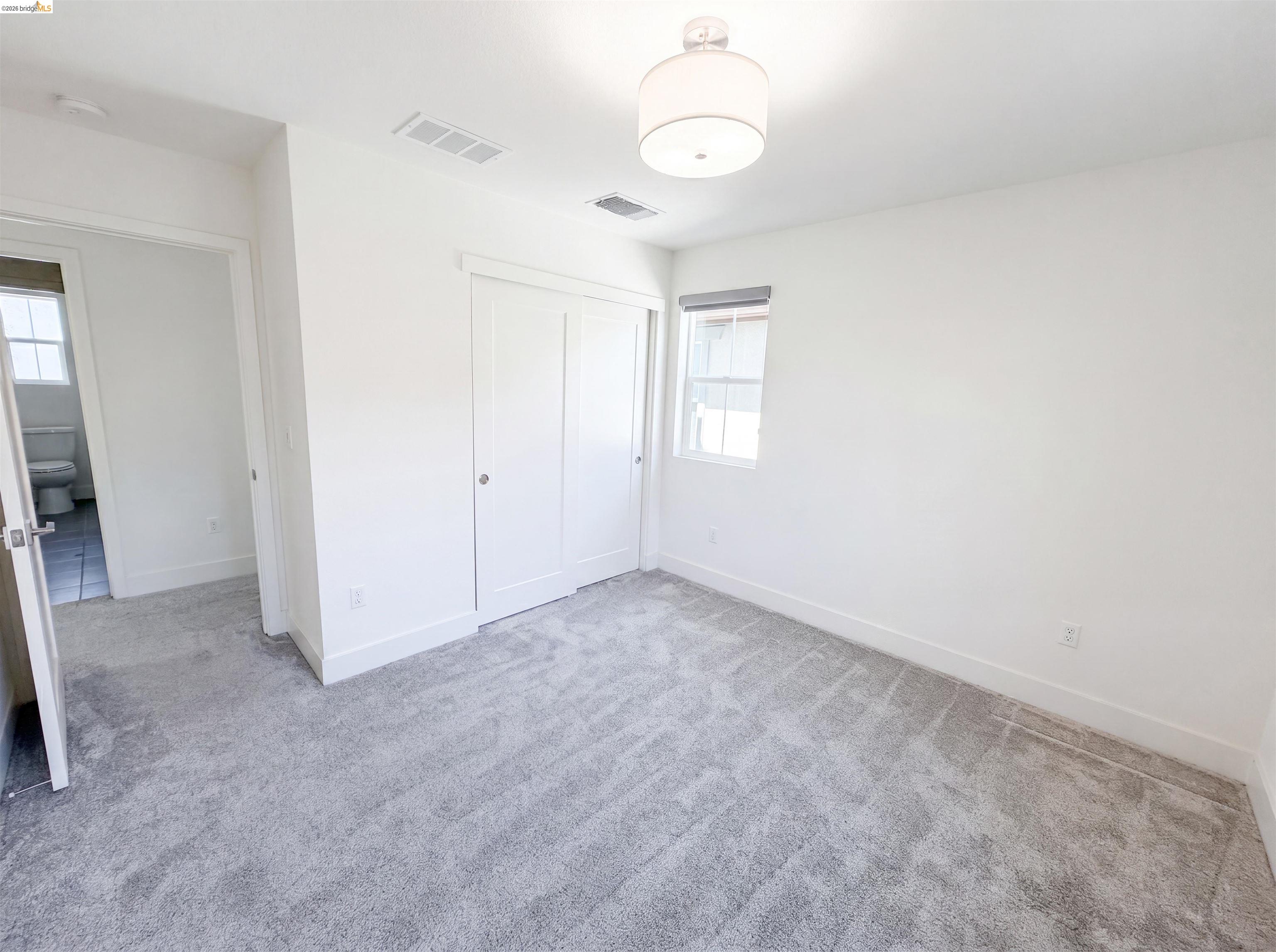 9034 Rudder Way Newark, CA 94560 - Photo 20 of 38 Spacious room featuring light gray patterned carpet, white walls, a single window, a semi-flush mount ceiling light, and white bi-fold closet doors