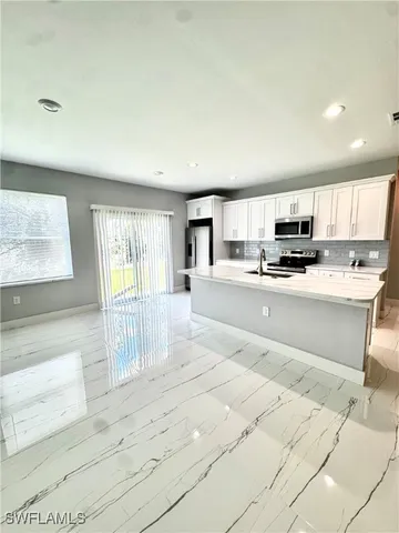 a large white kitchen with kitchen island a sink a counter top space and a window