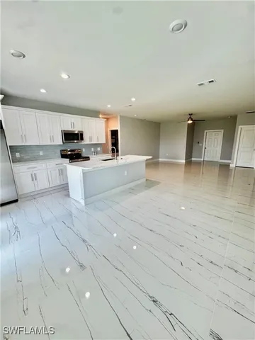 a large white kitchen with kitchen island a sink stainless steel appliances and cabinets