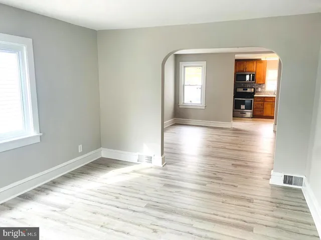a view of empty room with wooden floor and kitchen view
