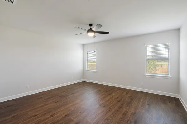 an empty room with wooden floor ceiling fan and windows