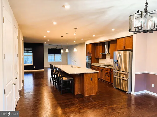 a kitchen with stainless steel appliances kitchen island granite countertop a refrigerator a stove top oven and cabinets with wooden floor