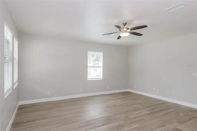 an empty room with wooden floor ceiling fan and window