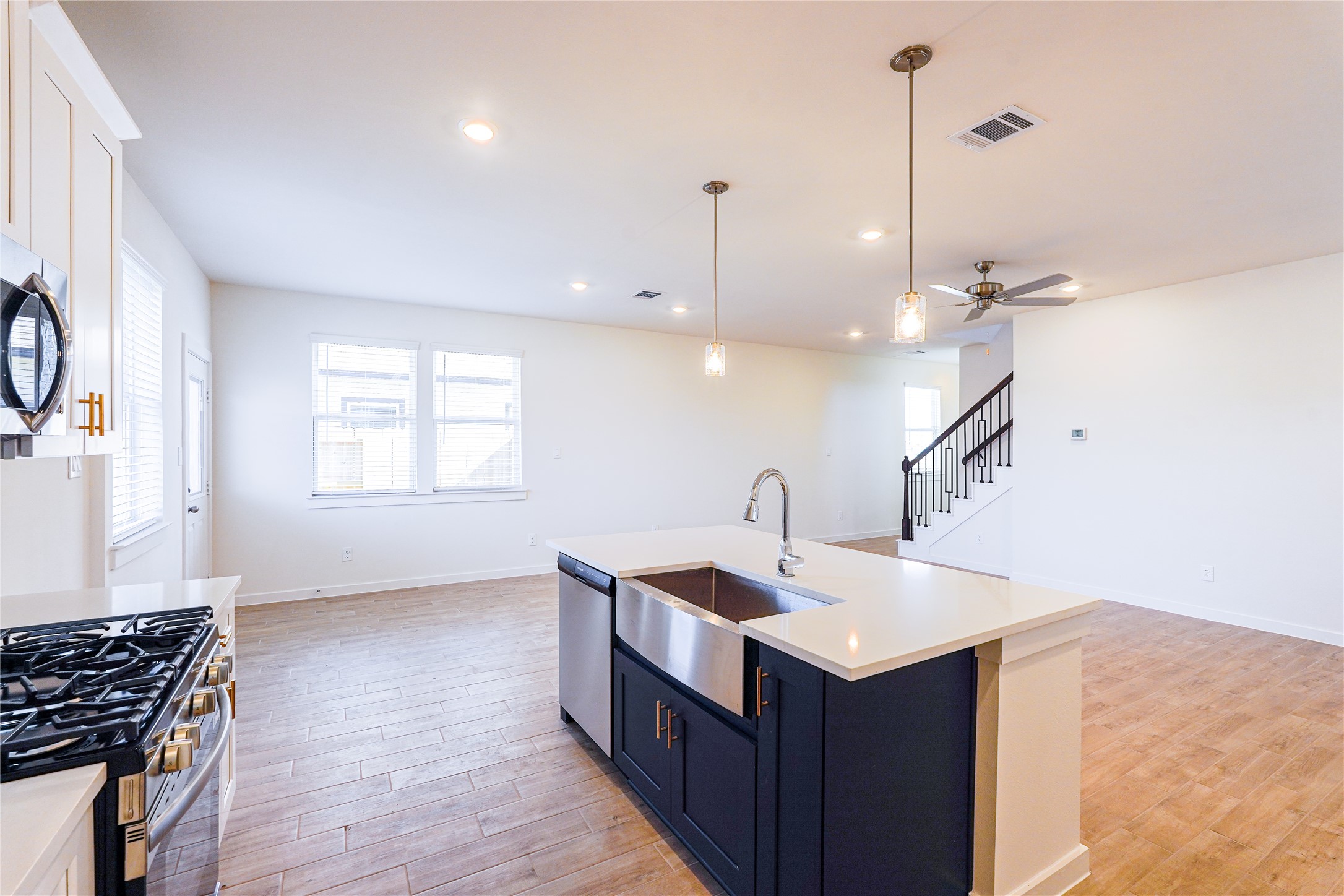6618 Escondido Drive Rosharon, TX 77583 - Photo 15 of 31 This photo showcases a spacious, open-concept kitchen and living area with modern finishes. It features a large island with a sink, pendant lighting, stainless steel appliances, and wood-style flooring. The room is bright with ample windows, and there's a staircase leading to the upper level.
