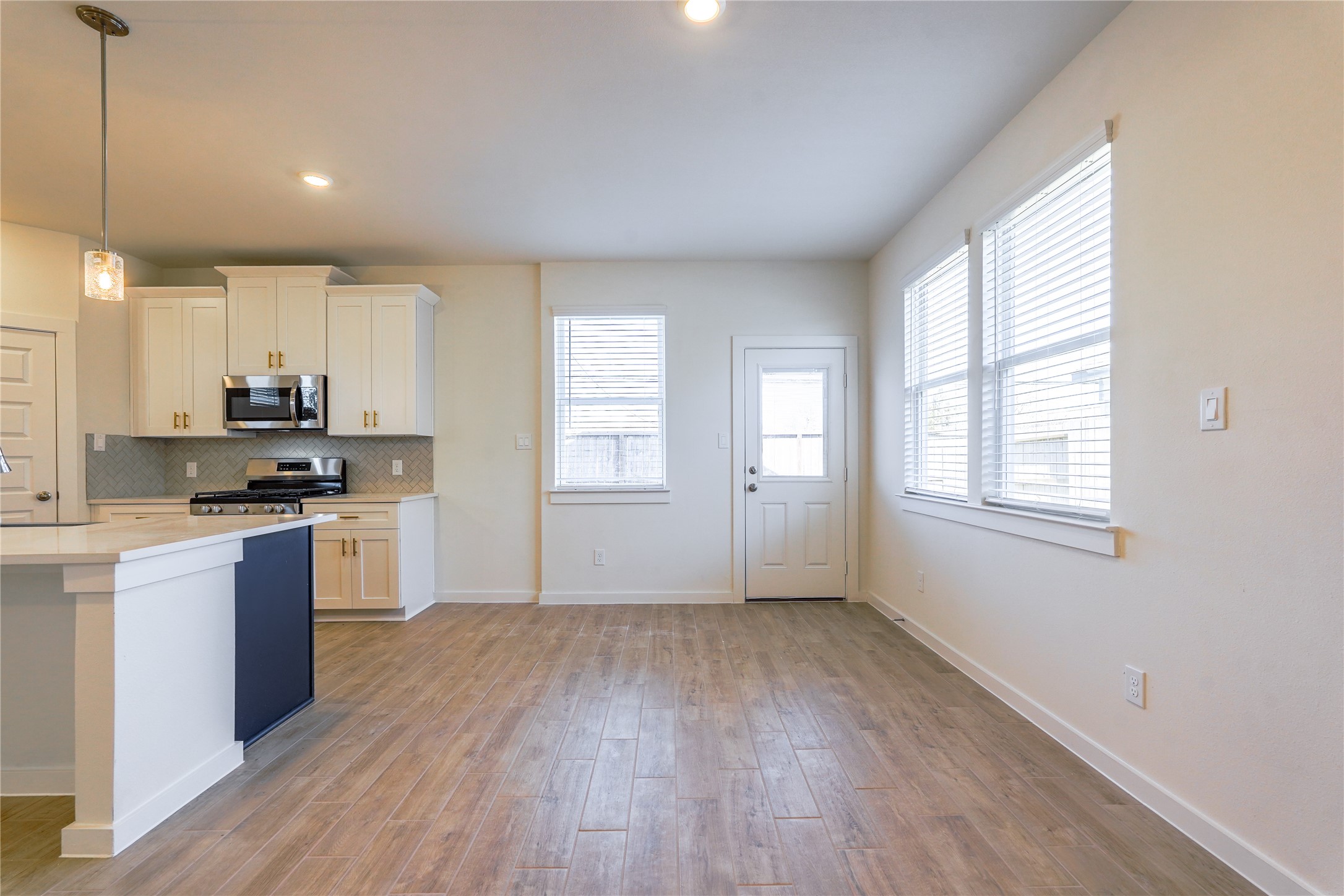 6618 Escondido Drive Rosharon, TX 77583 - Photo 16 of 31 This photo showcases a bright, open kitchen and dining area featuring modern white cabinetry, a gas stove, and hardwood floors. Large windows provide ample natural light, and there's a door leading outside, adding convenience and charm.