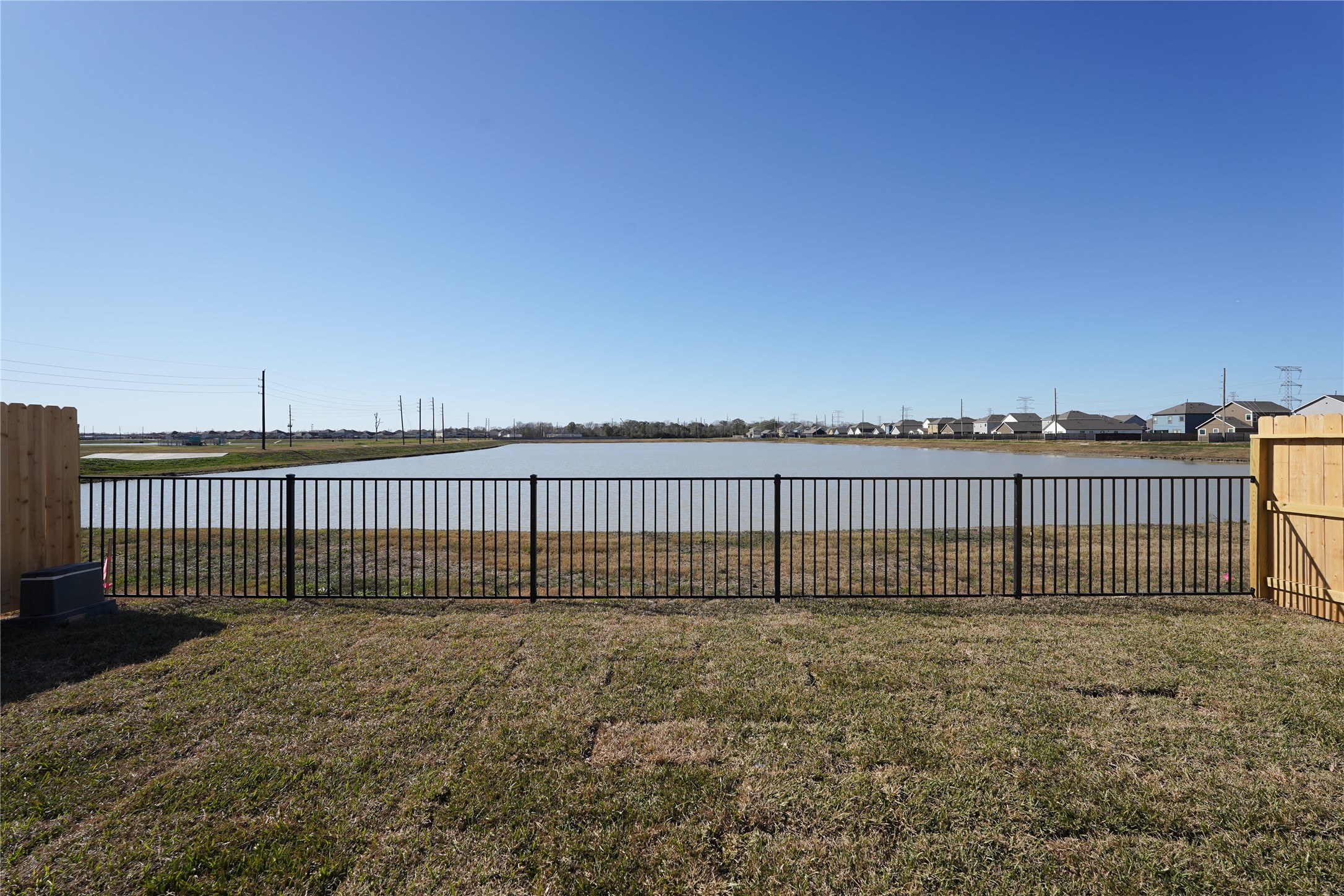 6618 Escondido Drive Rosharon, TX 77583 - Photo 26 of 31 The photo showcases a backyard with a metal fence overlooking a serene pond, offering a peaceful view and a spacious grassy area perfect for outdoor activities.
