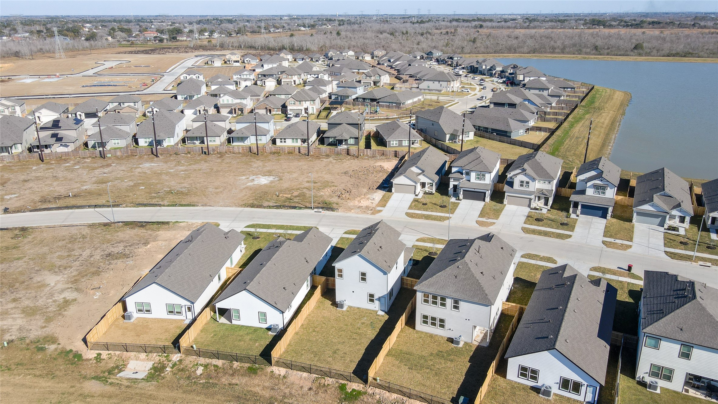 6618 Escondido Drive Rosharon, TX 77583 - Photo 30 of 31 This aerial photo showcases a suburban neighborhood with modern single-family homes. The area features neatly arranged houses with fenced yards, nearby roads, and a view of a small lake, providing a peaceful residential setting.
