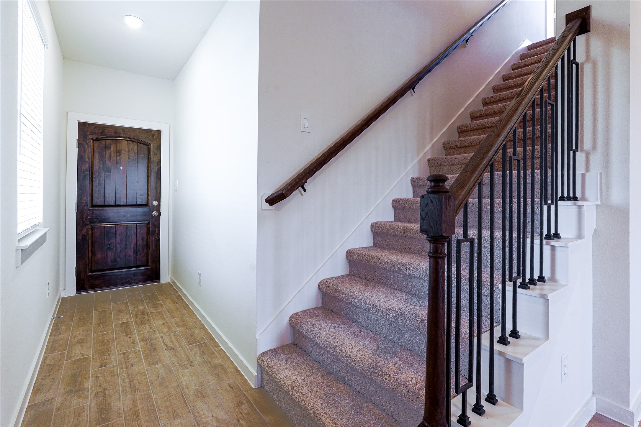 6618 Escondido Drive Rosharon, TX 77583 - Photo 4 of 31 Bright entryway featuring a dark wooden front door, wood-tile flooring, and a carpeted staircase with elegant railing, leading to the upper floor.