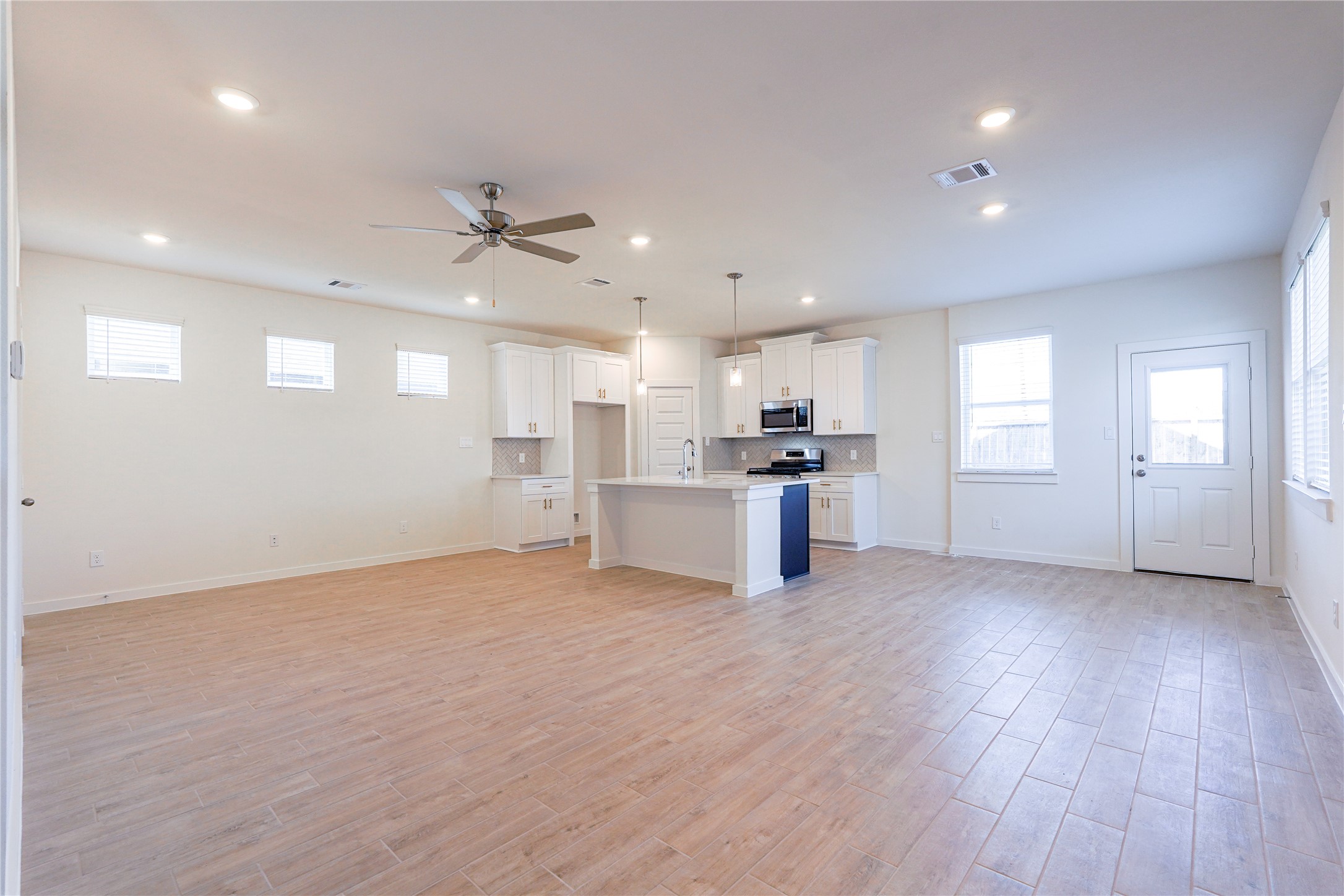 6618 Escondido Drive Rosharon, TX 77583 - Photo 7 of 31 This open-concept living space features modern hardwood flooring, recessed lighting, and a ceiling fan. The kitchen boasts white cabinetry, stainless steel appliances, and a central island with pendant lighting. Ample natural light comes through multiple windows, enhancing the bright and airy feel.