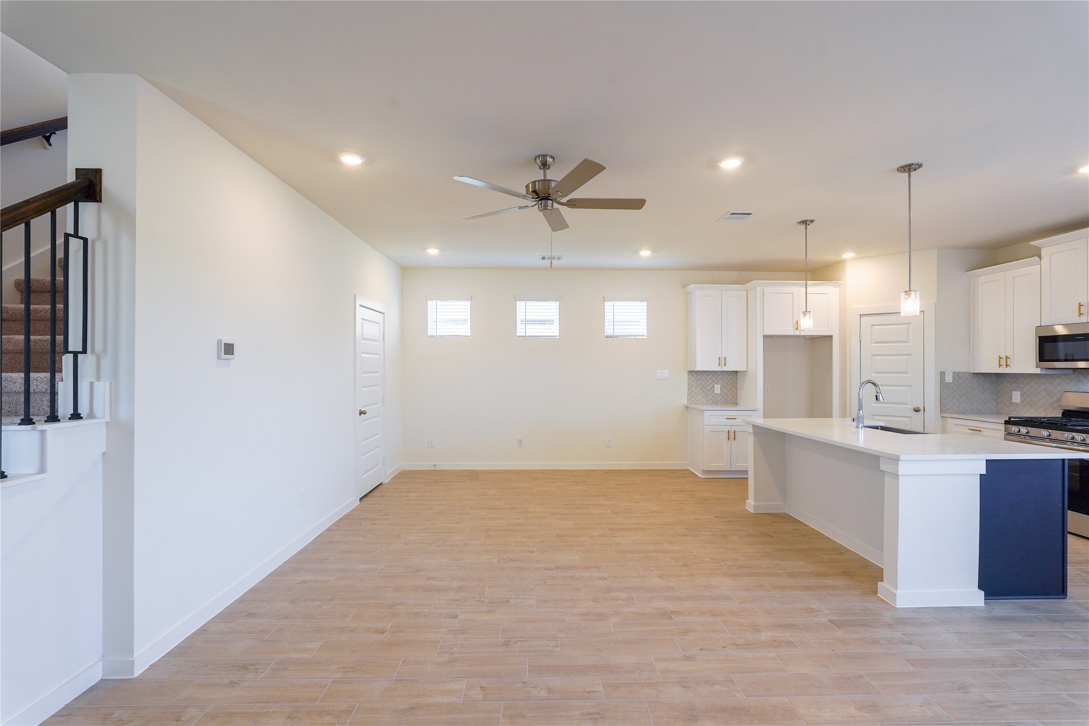 6618 Escondido Drive Rosharon, TX 77583 - Photo 9 of 31 This modern, open-concept space features a bright kitchen with white cabinetry, stainless steel appliances, and a large island with pendant lighting. The living area has wood flooring, recessed lighting, and a ceiling fan. A staircase with a stylish railing leads to the upper level, adding a touch of elegance.
