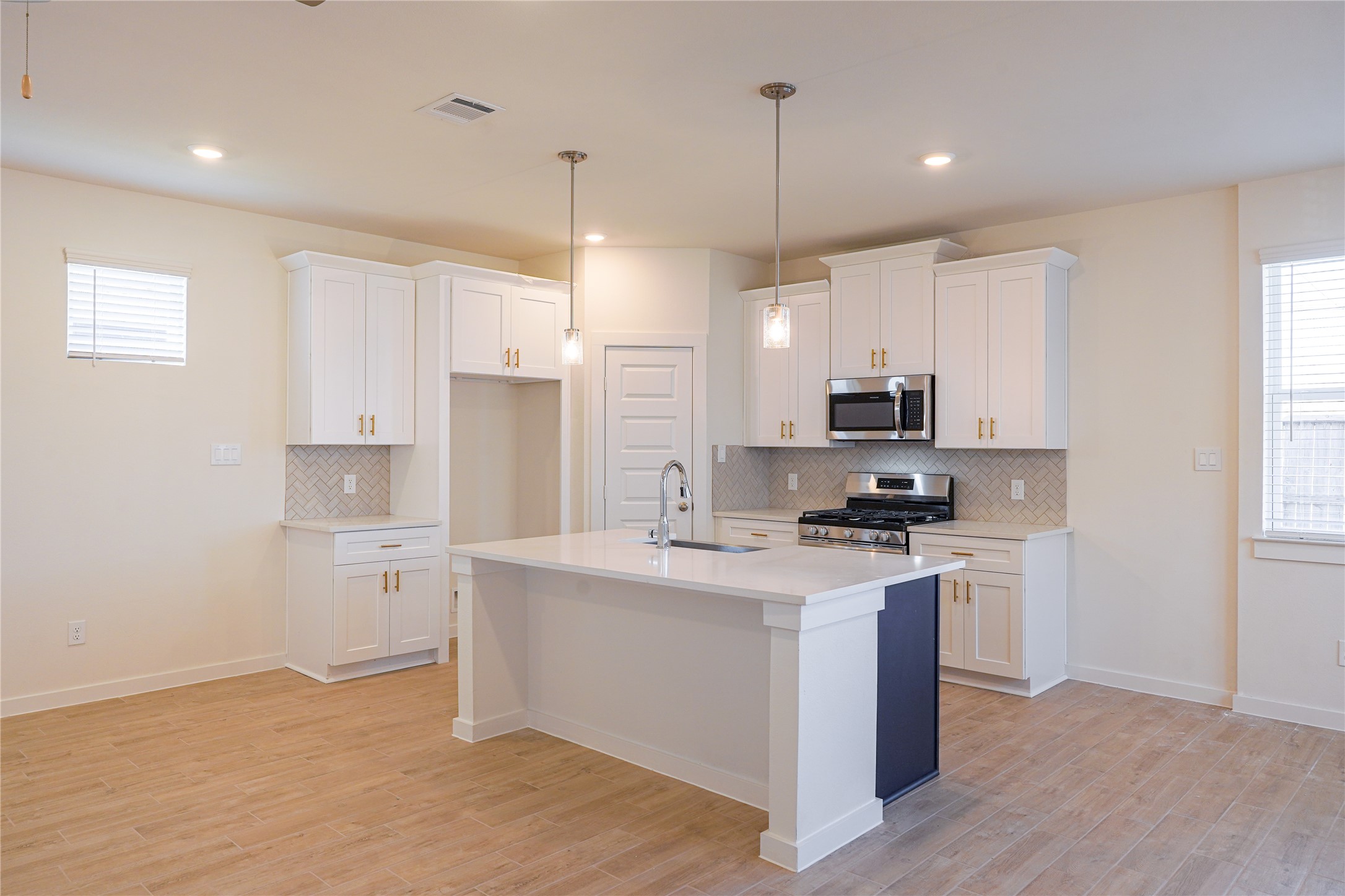 6618 Escondido Drive Rosharon, TX 77583 - Photo 10 of 31 This modern kitchen features a spacious island with a sink, white cabinets, pendant lighting, and stainless steel appliances. The light wood flooring and neutral walls create a bright, inviting space.