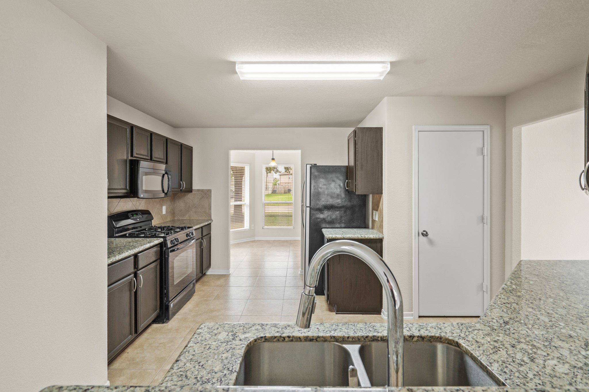 3118 Winchester Rnch Trail Katy, TX 77493 - Photo 7 of 22 The kitchen is well-equipped and ready for the whole family, featuring granite countertops, dark espresso cabinetry, a deep double stainless steel sink with pull-down faucet, gas range, built-in microwave, stainless steel refrigerator, and a tile backsplash — all with a clear view into the sunny breakfast area beyond.