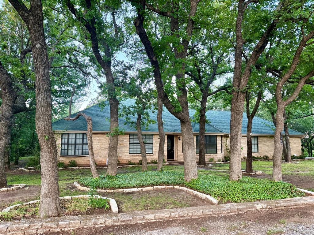 a view of a brick house with a yard plants and large tree