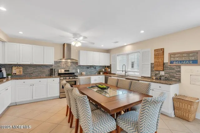 a kitchen with a sink dishwasher a stove a kitchen island with chairs and white cabinets