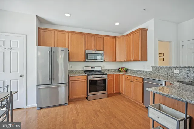 a kitchen with granite countertop wooden floors stainless steel appliances and a counter space