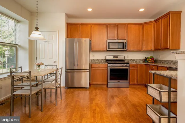 a kitchen with stainless steel appliances granite countertop a stove a refrigerator a sink a dining table and chairs with wooden floor