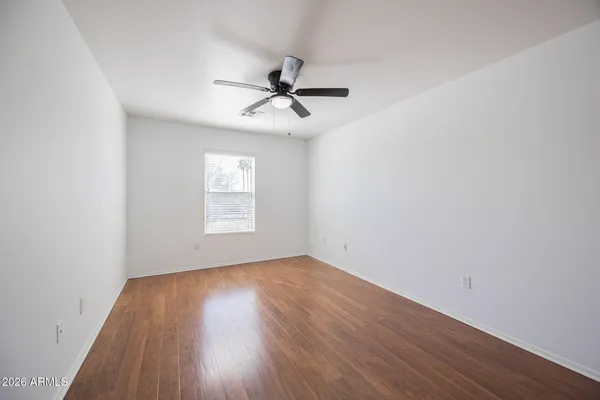an empty room with wooden floor ceiling fan and windows