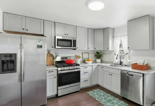 a kitchen with stainless steel appliances granite countertop a sink stove refrigerator and white cabinets with wooden floor