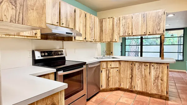 a kitchen with stainless steel appliances kitchen island wooden cabinets a stove a sink and a window