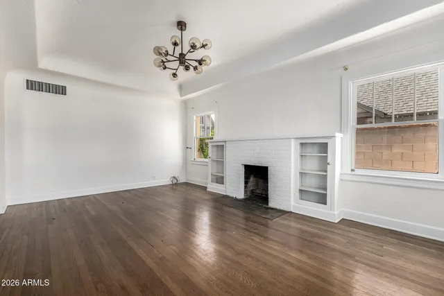 an empty room with wooden floor fireplace and windows